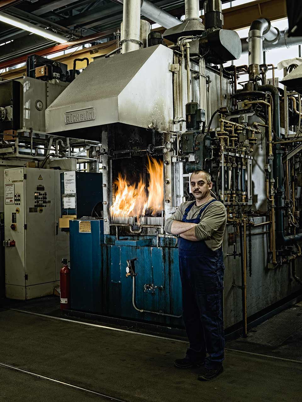 Industrie-Porträt eines Arbeiters vor brennendem Härteofen – Corporate Fotografie für authentische Unternehmensdarstellung in der Industrie